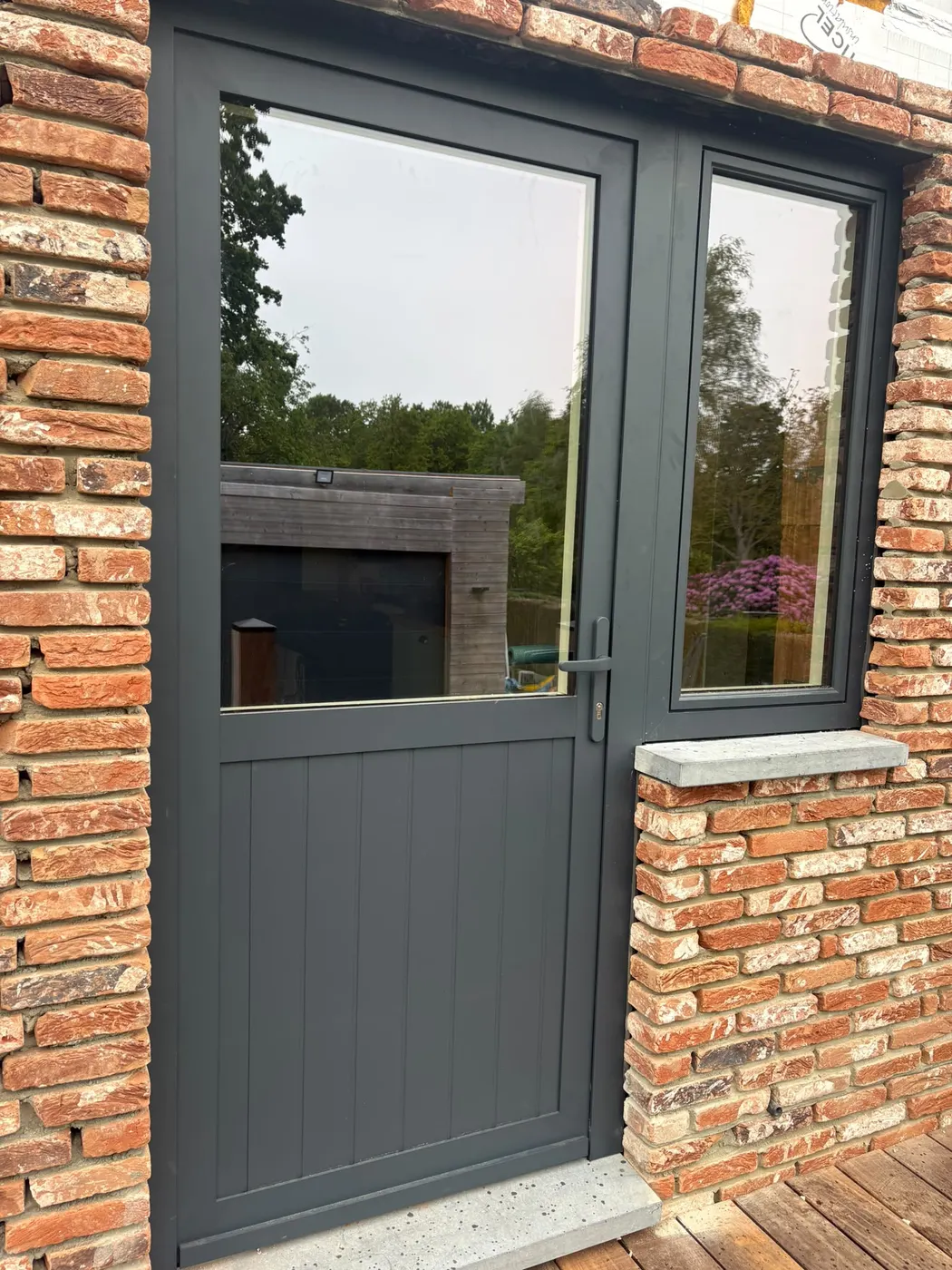 Antraciet deur met vast raam in een bakstenen gevel